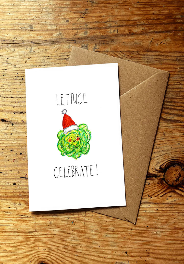Christmas card with lettuce character wearing a Santa hat and text 'LETTUCE CELEBRATE!' on a wooden surface.