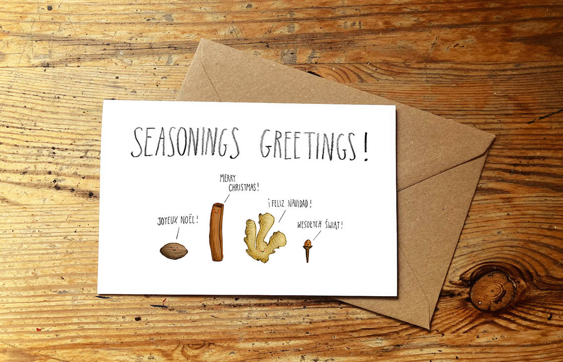 Christmas card with seasonings illustration and 'Seasonings Greetings!' text on a wooden surface.