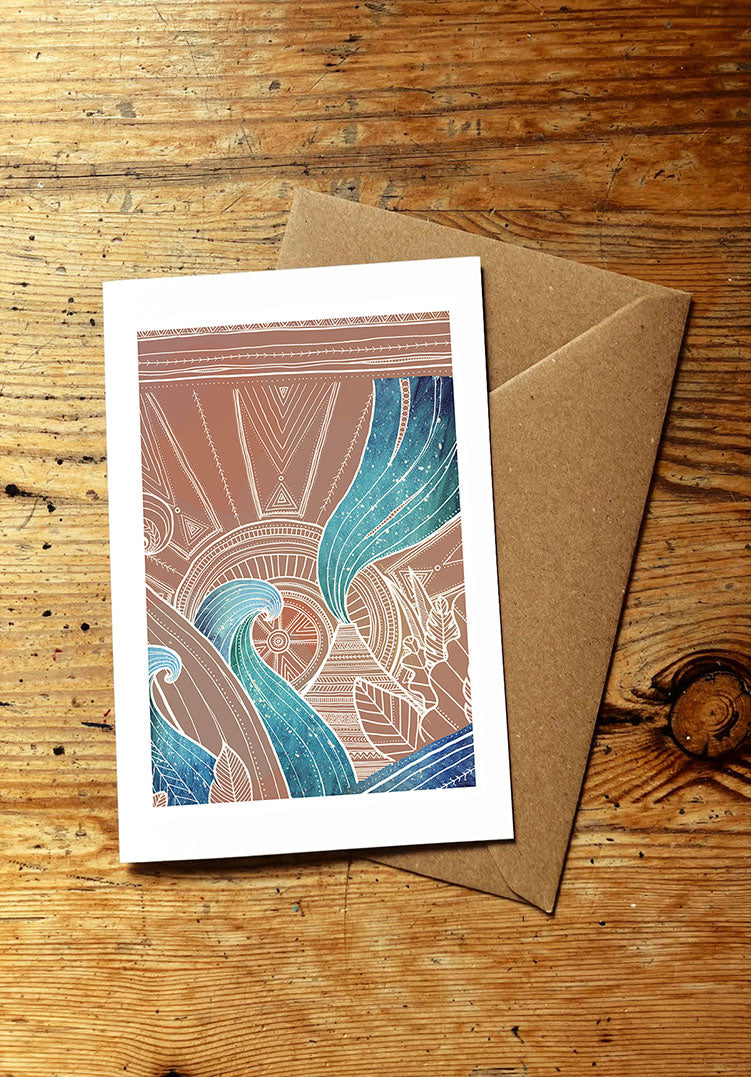 greeting card design with ocean waves, volcano, sun, and tropical plants, with a brown envelope on a wooden surface