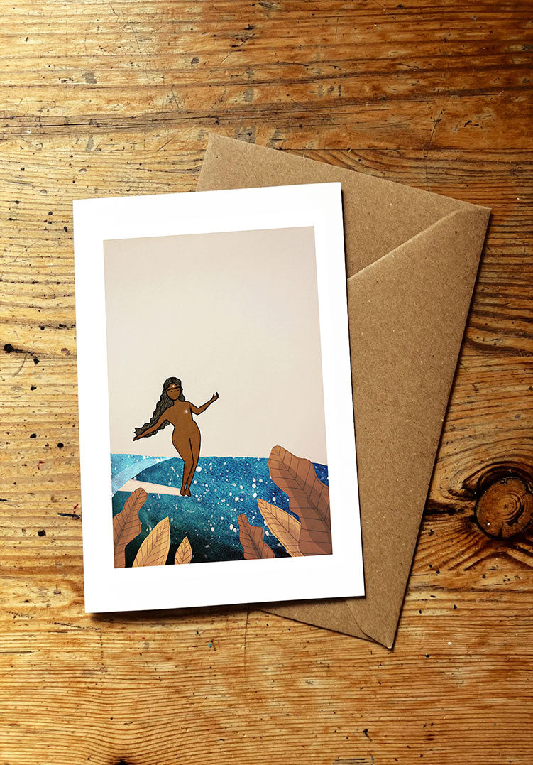 Greeting card with a surf girl surfing an ocean wave, and envelope on a wooden surface