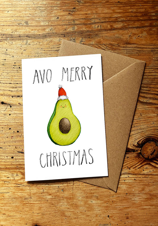 Christmas card with avocado wearing a Santa hat and text 'Avo Merry Christmas' on a wooden surface.