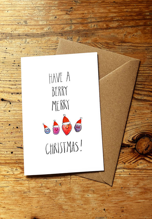 Christmas card with 'Have a Berry Merry Christmas!' text and berries wearing santa hats, on a wooden surface.