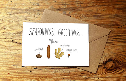 Christmas card with seasonings illustration and 'Seasonings Greetings!' text on a wooden surface.