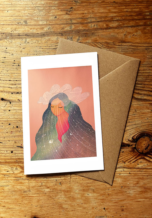 Greeting card with a surreal design of a woman with long hair with stars and planets in it and a cloud on her head, on a wooden surface