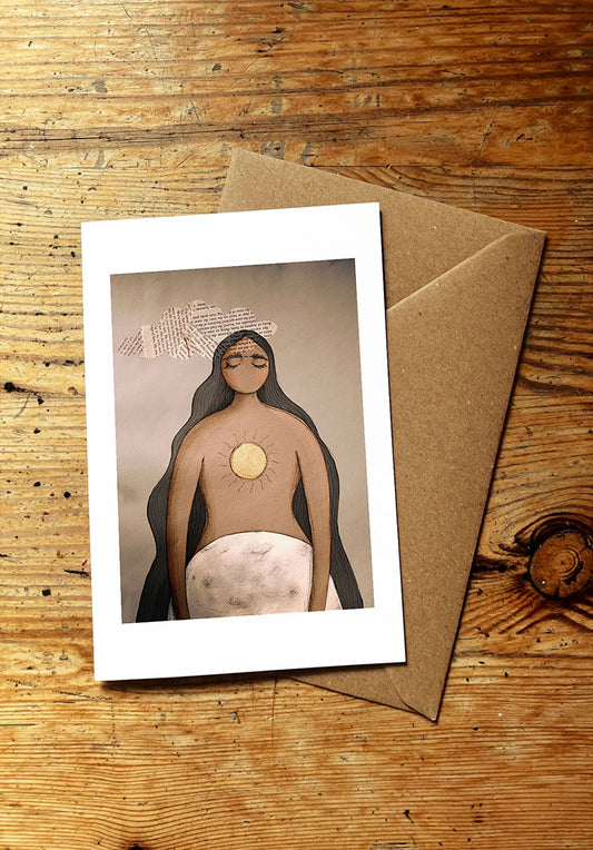 Greeting card with an illustration of a woman with a sun symbol on her chest, holding a moon, placed on a wooden surface with a brown envelope.