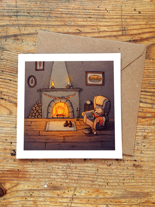 Greeting card with a hedgehog sitting in an armchair and cozy fireplace scene on a wooden surface