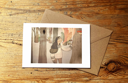 Greeting card with illustration of a woman in a forest and envelope on a wooden surface