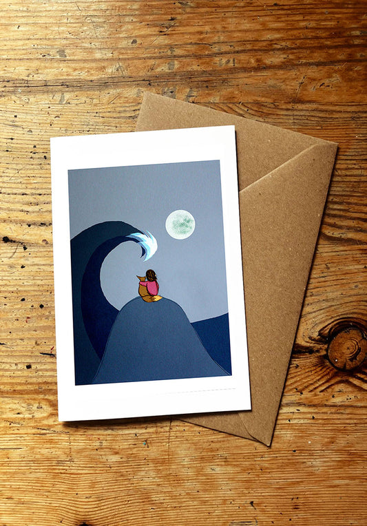 Greeting card with a wave and moon design and a fox and a girl on a wooden surface