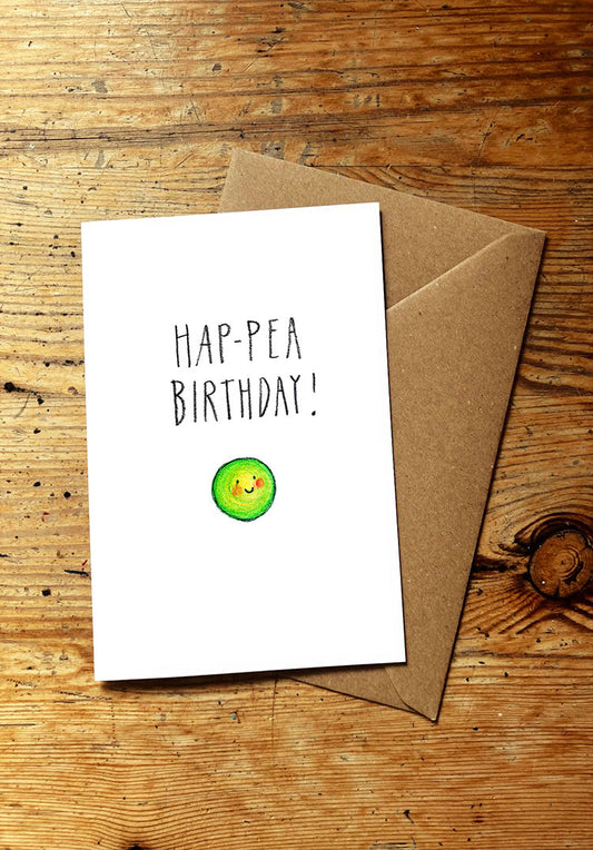 Veg pun greeting card with 'Hap-Pea Birthday!' text and a smiley green pea illustration on a wooden surface.