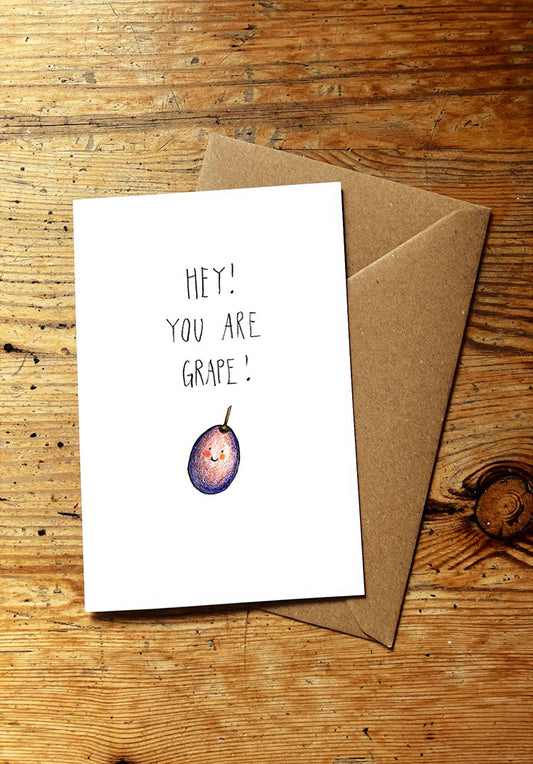 Fruit and veg pun greeting card with 'Hey! You are grape!' text and a smiley grape illustration on a wooden surface.