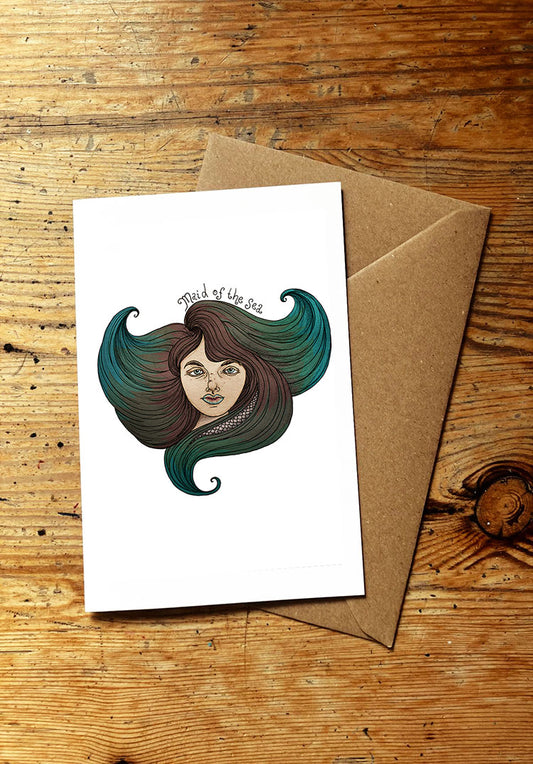 Greeting card with a stylized illustration of a woman's face with flowing hair like ocean waves on a wooden surface with a brown envelope.