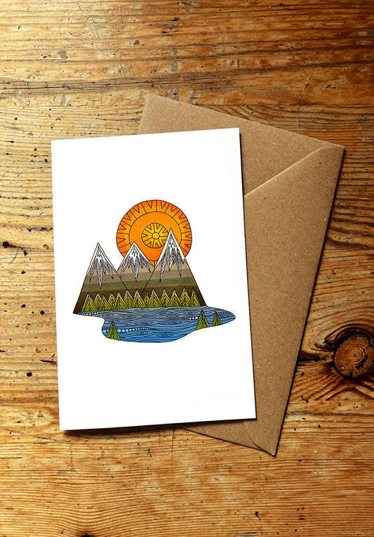 Greeting card with mountain and sun design on a wooden surface