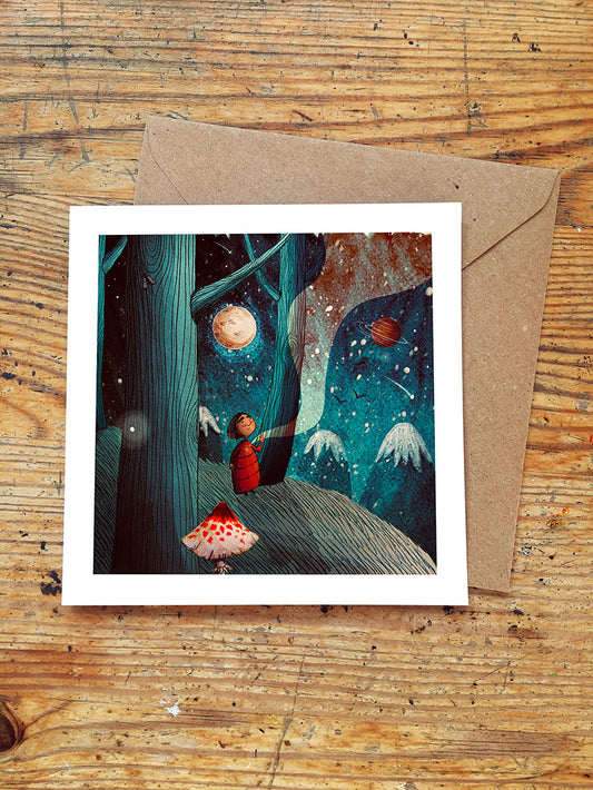 Greeting card with a child on a forested hillside looking up at the starry night sky with moon and planets and red mushroom on a wooden surface