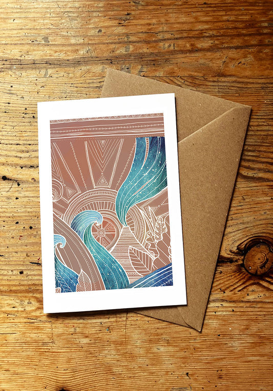 greeting card design with ocean waves, volcano, sun, and tropical plants, with a brown envelope on a wooden surface