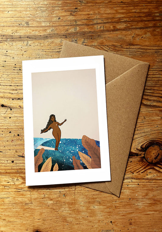 Greeting card with a surf girl surfing an ocean wave, and envelope on a wooden surface