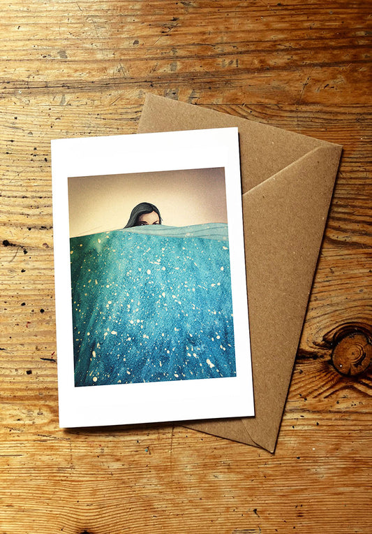 Greeting card with a woman swimming in the sea and a brown envelope on a wooden surface